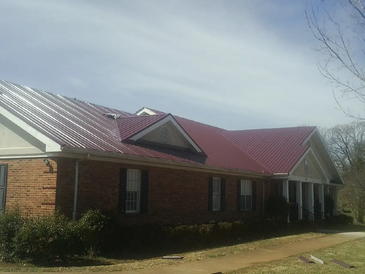 Red metal roof with gabled entries on a long brick building, from a Hail Damage Roof Repair job in Newport