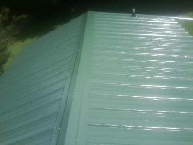 New green metal panels meeting at the ridge of a roof — Flat Roof Repair work by our crew in Newport